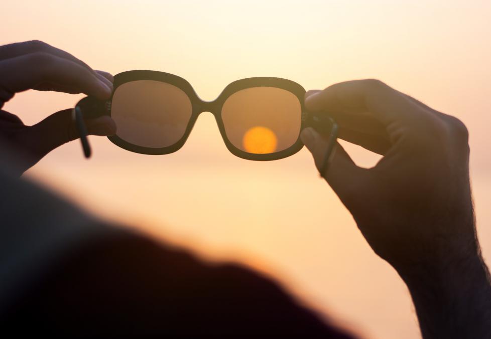Use these tips to make sure your sunglasses truly protect your eyes. Person holding sunglasses up to sky.