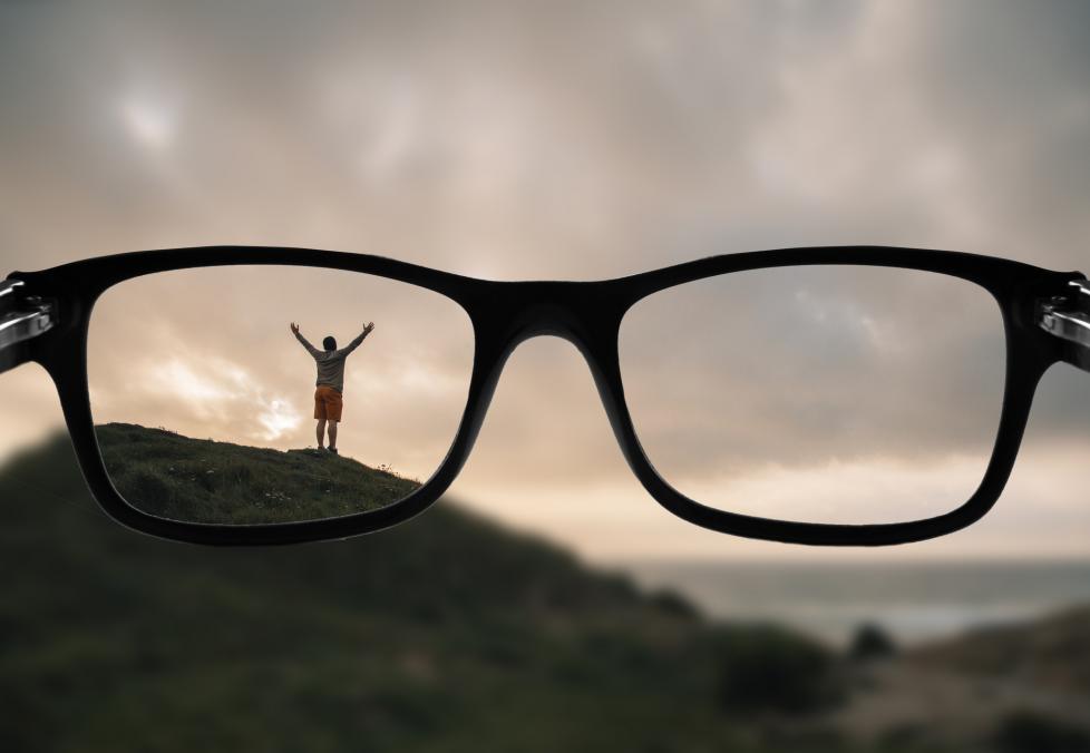 A first-person POV of someone looking through glasses at a person standing on a hill
