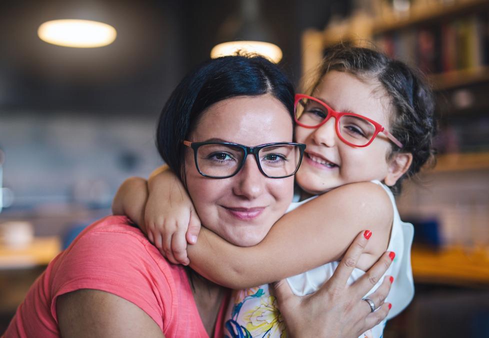 Mom and daughter wearing glasses hugging.