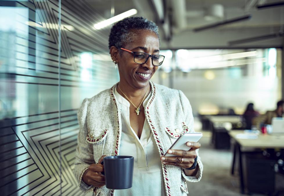 African American woman wearing glasses looking at phone smiling