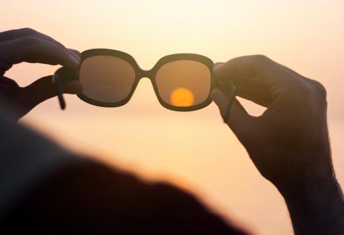 Use these tips to make sure your sunglasses truly protect your eyes. Person holding sunglasses up to sky.
