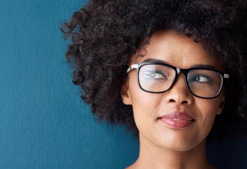 Thinking of ways to use her tax refund on eye care is this young woman wearing glasses looking thoughtful against a blue background.