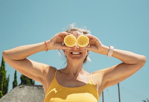 An older woman holding up orange slices to her eyes