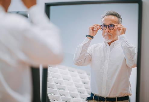 Middle-aged man trying on glasses in front of a mirror for a story on how to find glasses for your face shape
