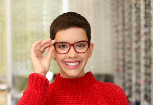 Smiling young adult woman trying on glasses for a story on the best glasses for oval face shape