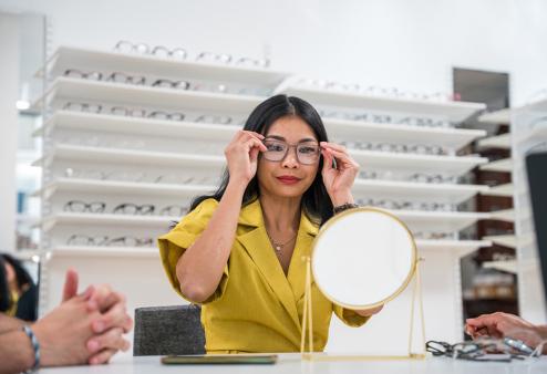 Young adult female trying on glasses for a story on the best glasses for round faces